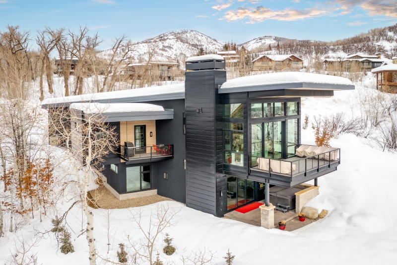 Modern dark-clad mountain home in winter with glass walls